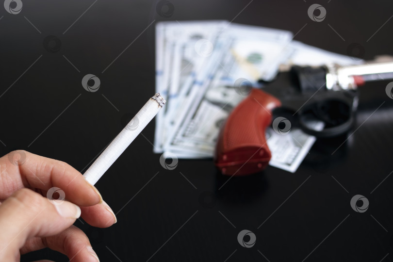 Скачать Пистолет, доллары и рука с сигаретой на деревянном столе фотосток Ozero