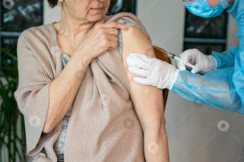 Скачать Пожилой женщине вводят вакцину в плечо. Вакцинация против коронавируса. Вакцинация старого пациента в клинике с копировальным пространством. Врач делает укол пожилой женщине в больнице фотосток Ozero