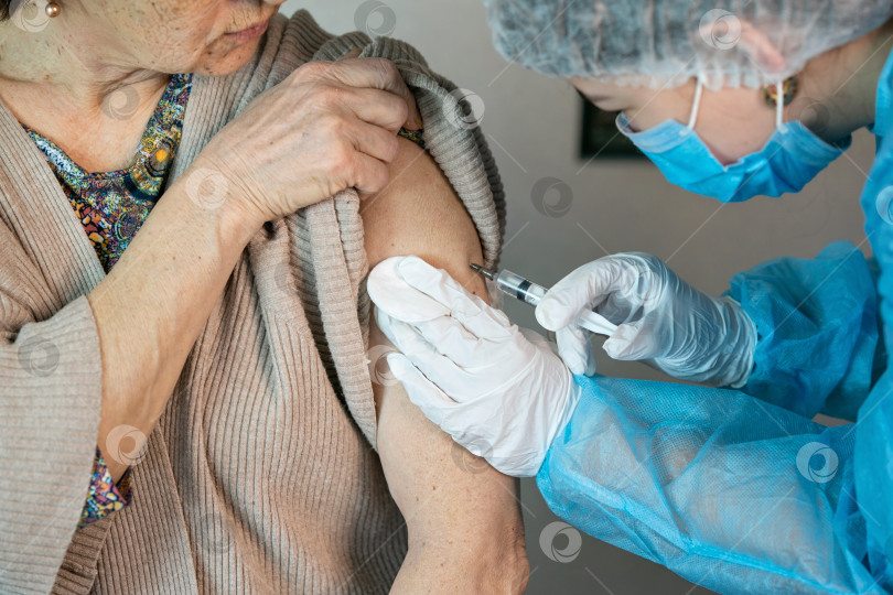 Скачать Пожилой женщине вводят вакцину в плечо. Вакцинация против коронавируса. Вакцинация старого пациента в клинике с копировальным пространством. Врач делает укол пожилой женщине в больнице фотосток Ozero