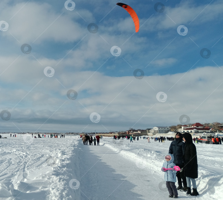 Скачать Семья восторженно наблюдает за ярким  парусом, в небе парящем, во время прогулки по затянутому льдом Жигулевскому морю в день чемпионата России по сноукайтингу фотосток Ozero