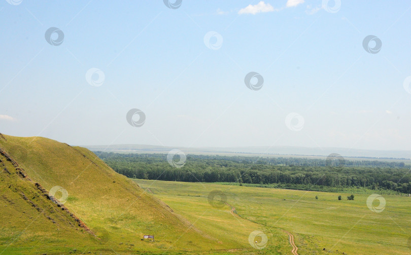 Скачать Фрагмент склона высокой горы с необычными каменными образованиями на краю бескрайней степи в солнечный летний день. фотосток Ozero