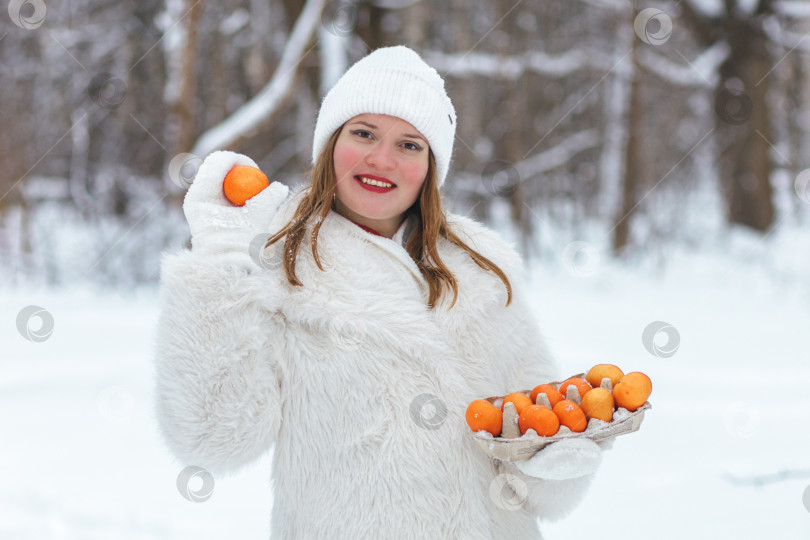 Скачать Оранжевые мандарины лежат в картонной экологически чистой коробке из-под куриных яиц. Женские руки на улице с коробкой мандаринов в руках фотосток Ozero