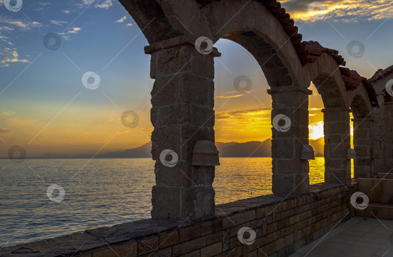 Скачать Вид на закат и море сквозь стену, сложенную из каменных арок. фотосток Ozero