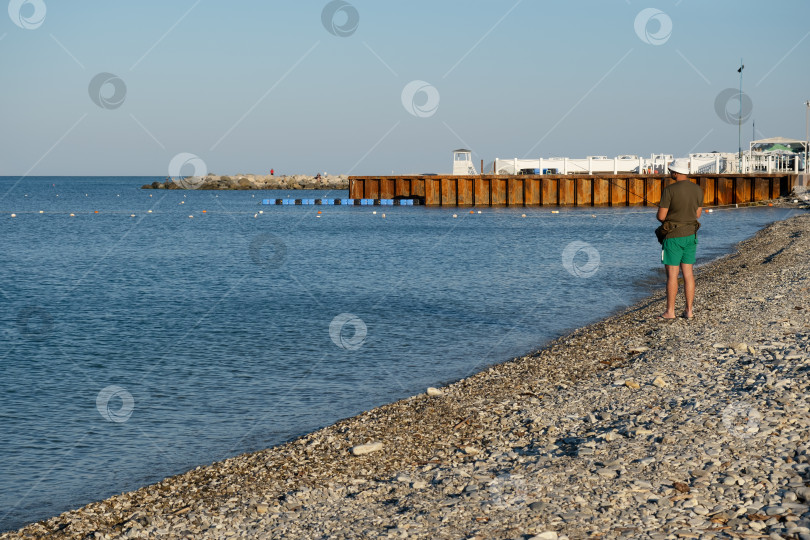 Скачать Морская сцена с видом сзади на мужчину, ловящего рыбу с галечного пляжа в бухте курортного поселка Небуг, Краснодарский край, Россия. фотосток Ozero