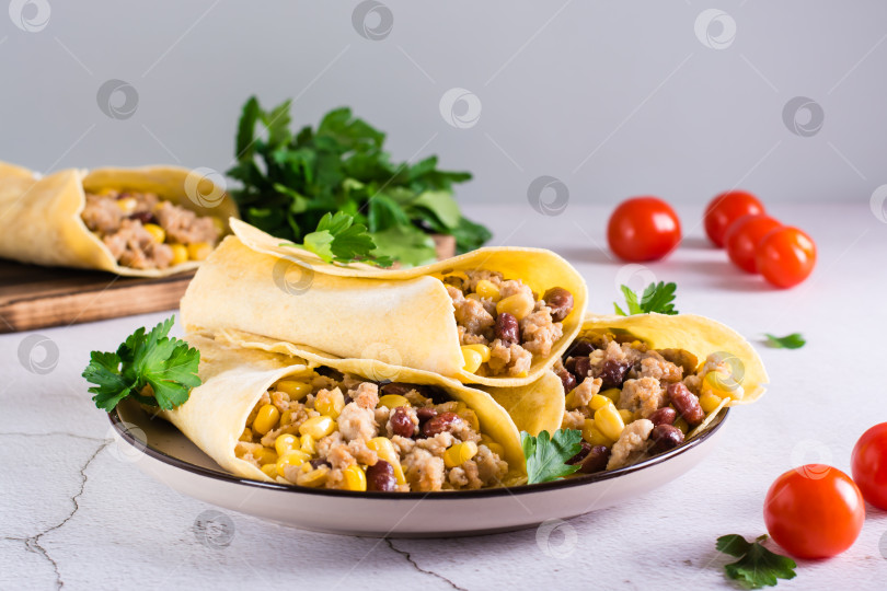 Скачать Буррито с мясным фаршем, кукурузой, фасолью и помидорами в кукурузных тортильях на тарелке на столе фотосток Ozero
