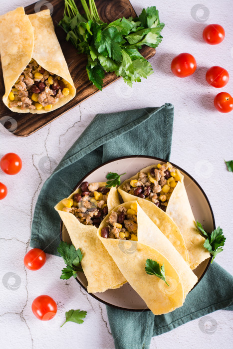 Скачать Традиционные мексиканские буррито с мясным фаршем, кукурузой и фасолью на тарелке. Вид сверху и по вертикали фотосток Ozero
