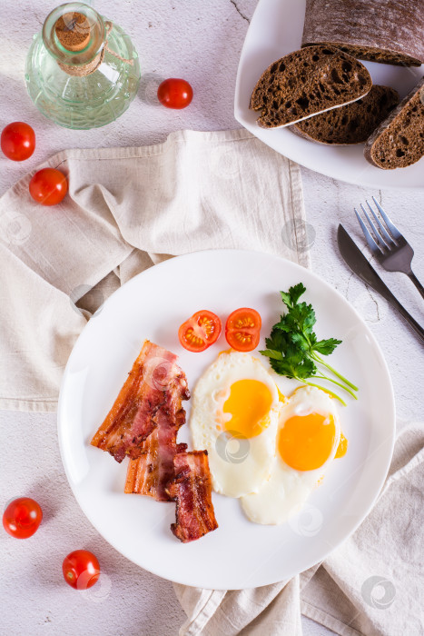 Скачать Домашний завтрак с яичницей с беконом, помидорами и зеленью на тарелке. Вид сверху и по вертикали фотосток Ozero