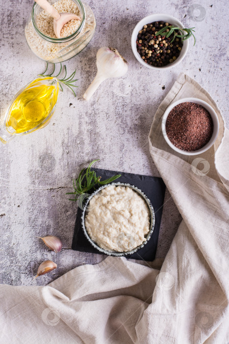 Скачать Тахини с кунжутом и черной солью в миске и ингредиенты для приготовления на столе. Вид сверху и по вертикали фотосток Ozero