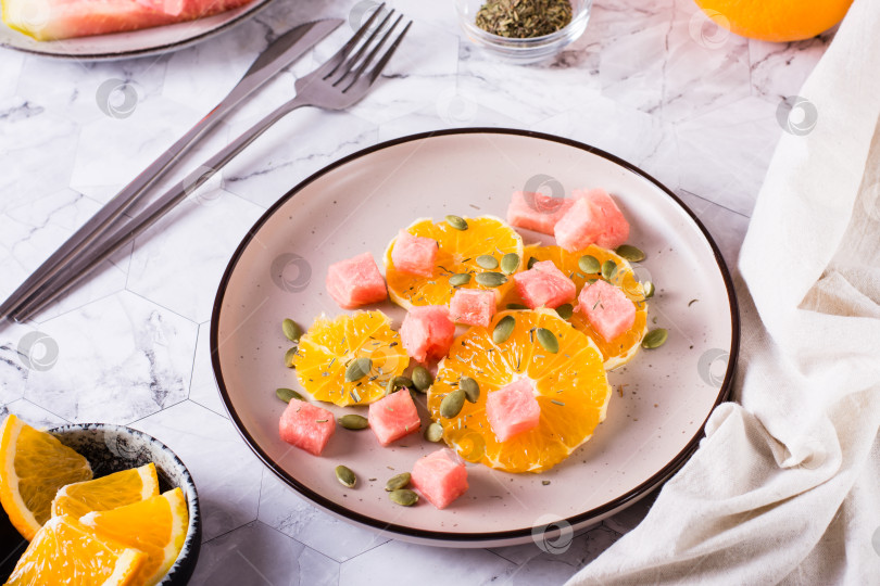 Скачать Свежий салат из апельсина, арбуза и тыквенных семечек на тарелке на столе. Органическая диета. фотосток Ozero
