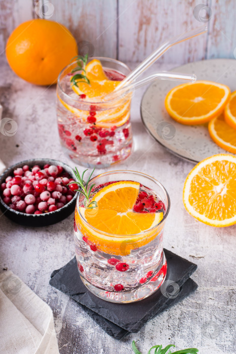 Скачать Крепкий сельтерский коктейль с ягодами, апельсином, розмарином и льдом в бокалах на столе. Вертикальный вид фотосток Ozero