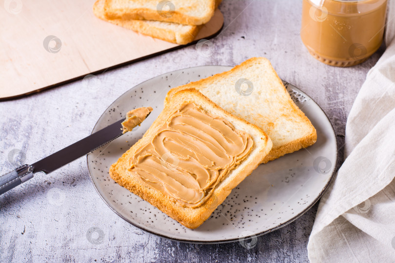 Скачать Хлебные тосты с арахисовым маслом на тарелке и баночка сливочного масла на столе фотосток Ozero