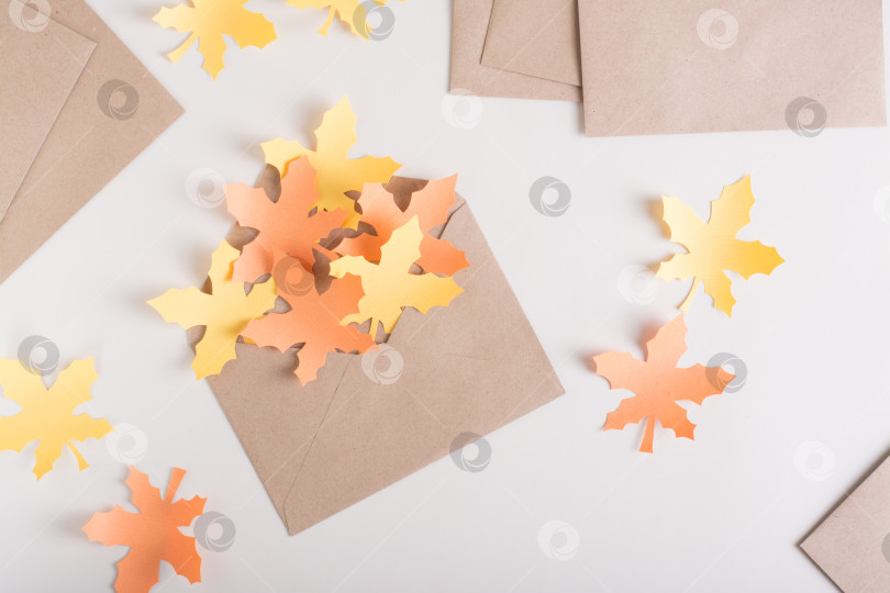 Скачать Бумажные желтые и оранжевые кленовые листья в крафтовом конверте на розовом фоне. Вид сверху. фотосток Ozero