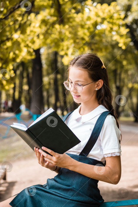 Скачать Школьница в очках читает книгу теплым днем в парке. Вертикальный вид фотосток Ozero