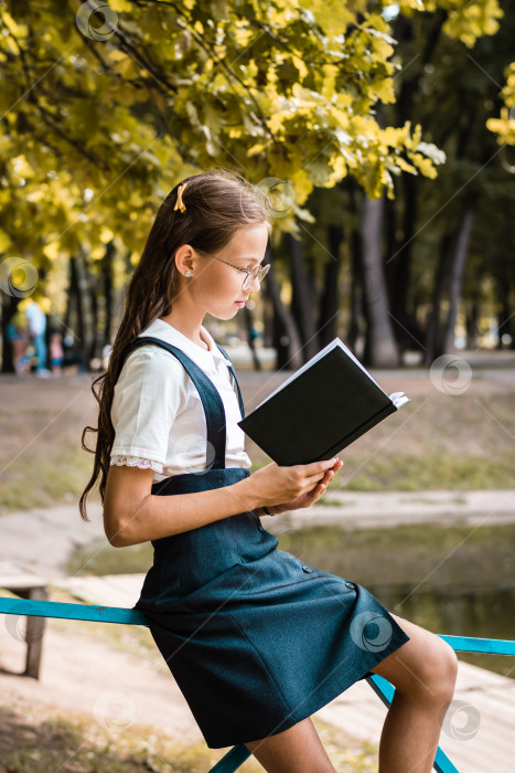 Скачать Девочка-подросток в школьной форме читает книгу теплым днем в парке. Вертикальный вид фотосток Ozero