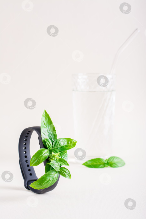 Скачать Свежие листья на экране фитнес-браслета и стакане воды. Концепция заботы о здоровье, жизненной силы. Вертикальный вид фотосток Ozero