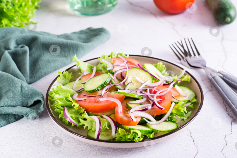 Скачать Салат из помидоров, огурцов, лука, листьев салата-латука на тарелке на столе. Вегетарианская еда фотосток Ozero