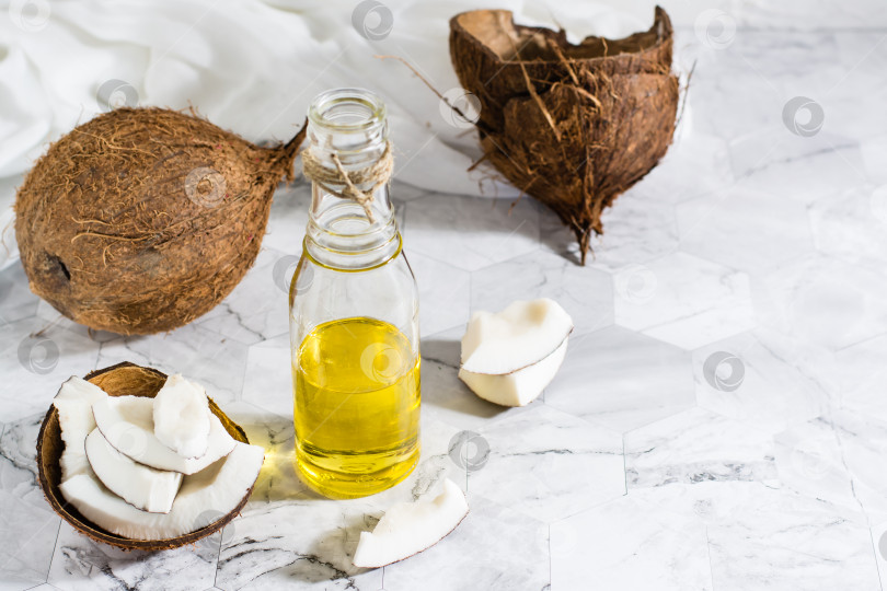Скачать Свежее растительное кокосовое масло в бутылке и кусочки кокоса на столе. Скопировать пробел фотосток Ozero