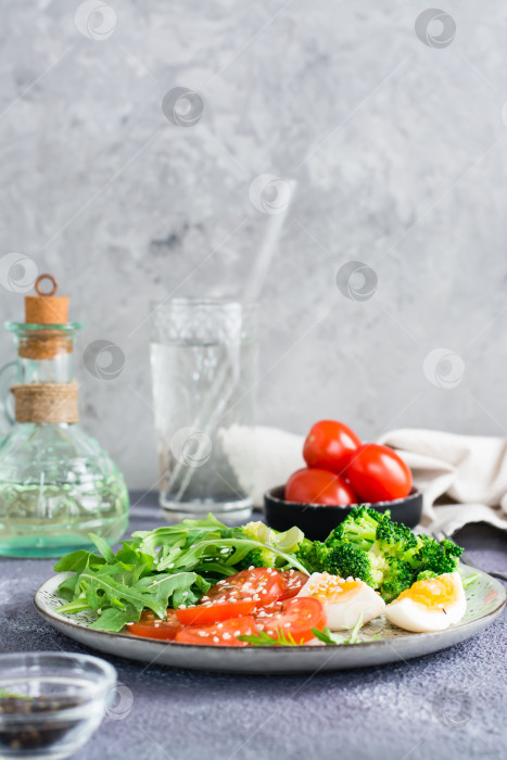 Скачать Тарелка с брокколи, помидорами, рукколой, вареным яйцом и семенами кунжута на тарелке. Вертикальный вид фотосток Ozero