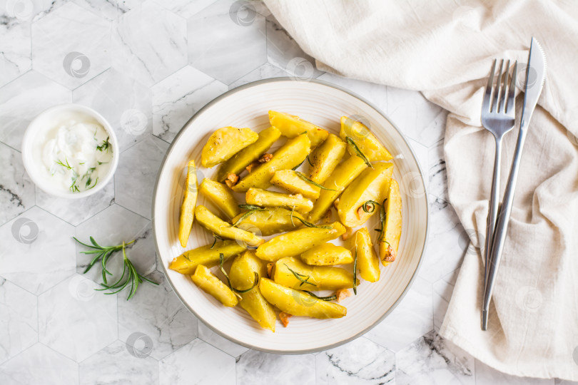 Скачать Запеченный картофель с чесноком и розмарином на тарелке и миска с соусом на столе. Вид сверху фотосток Ozero