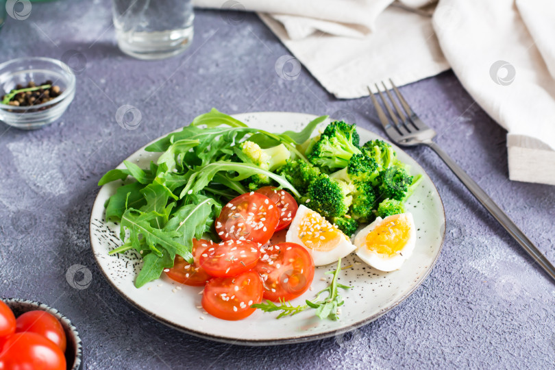 Скачать Тарелка с брокколи, рукколой, помидорами и вареным яйцом на тарелке на столе. Кетогенная диета фотосток Ozero