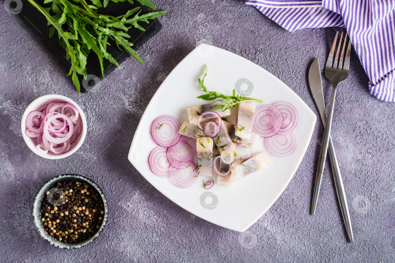 Скачать Нарезанная соленая сельдь с луком и рукколой на тарелке на столе. Простая закуска. Вид сверху фотосток Ozero