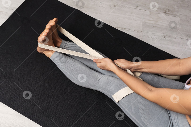 Скачать Женщина выполняет упражнение для растяжки мышц ног с помощью ремней, тренируясь сидя на коврике в спортивной одежде фотосток Ozero