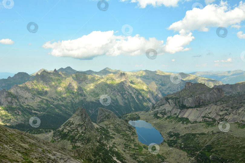 Скачать Вид сверху на скалу необычной причудливой формы и живописное озеро у подножия, окруженное высокими горами в солнечный летний день. фотосток Ozero