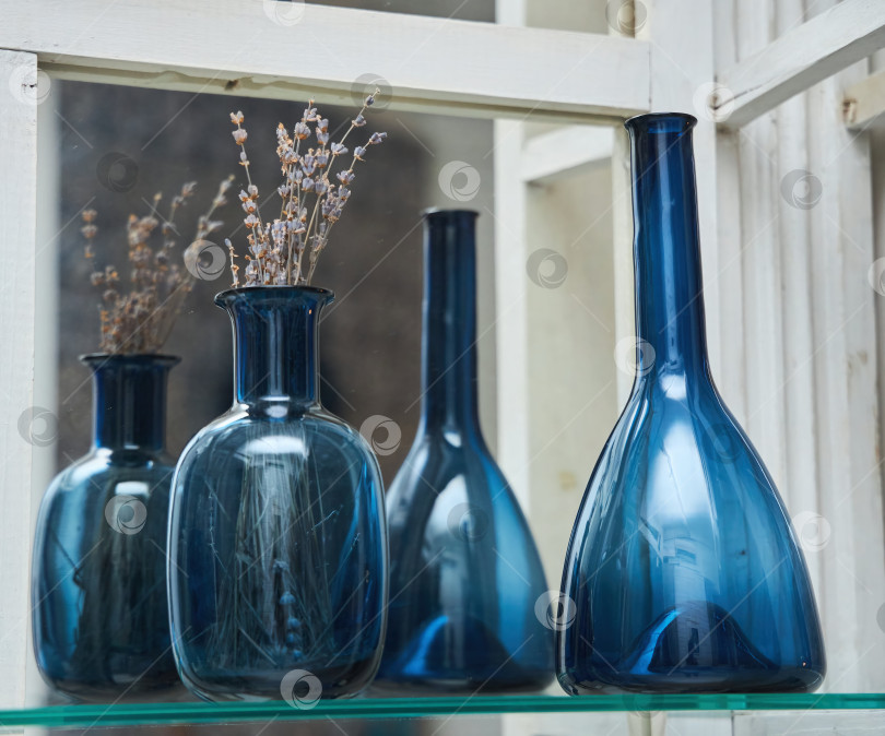 Скачать На полке стоит голубая стеклянная ваза с сухим растением. Рядом с ней кувшин из того же материала. Восточный декор. фотосток Ozero