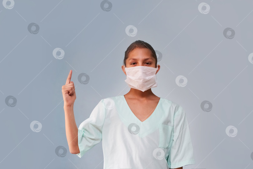 Скачать В кадр заглядывает молодая медсестра или ассистент в медицинской одежде и маске. фотосток Ozero
