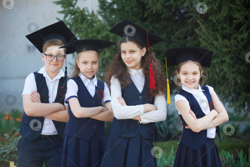 Скачать Три девочки и мальчик - выпускники начальной школы в шапочке выпускника и школьной форме. фотосток Ozero
