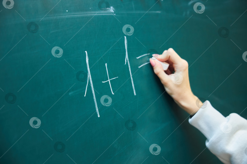 Скачать Рука подростка мелом пишет простой математический пример на зеленой доске. Концепция образования и дрессировки. фотосток Ozero