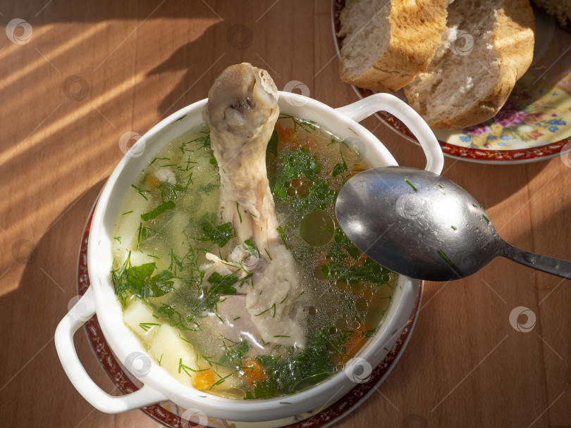 Скачать Аппетитный куриный суп на обед. На поверхности куриного супа видна зелень и капельки жира. На столе в тарелке лежат кусочки хлеба. фотосток Ozero