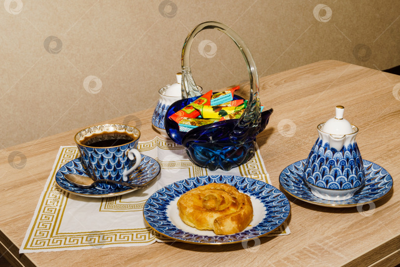Скачать Чашка кофе, булочка "Улитка", чайник, ваза с конфетами на столе фотосток Ozero