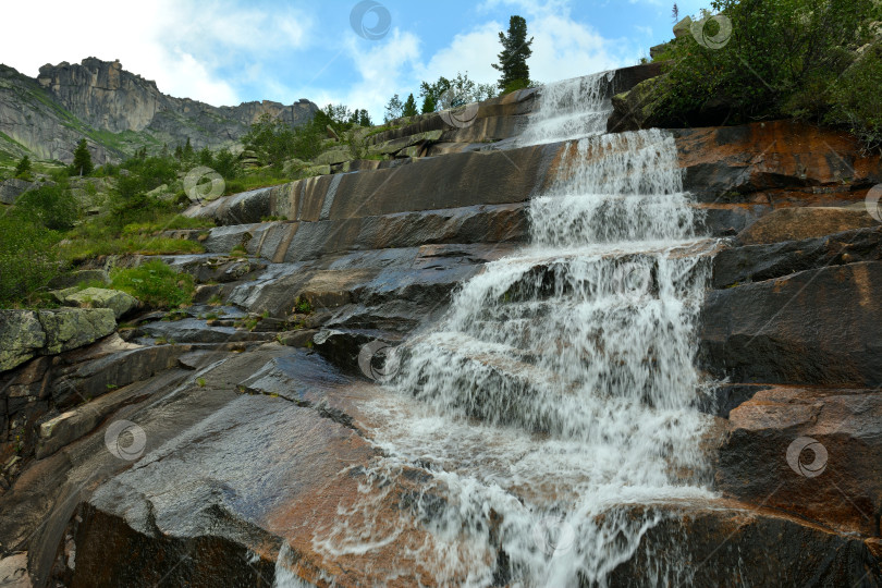 Скачать Каменные ступени горы образуют водопад для бурной горной реки в солнечный летний день в тайге. фотосток Ozero