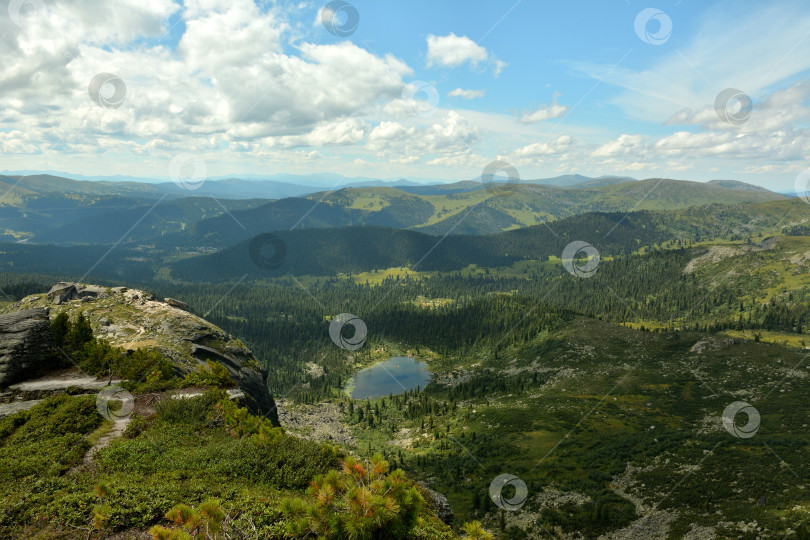 Скачать Вид с вершины горы на густую тайгу на хребтах и небольшое живописное озеро в низине. фотосток Ozero