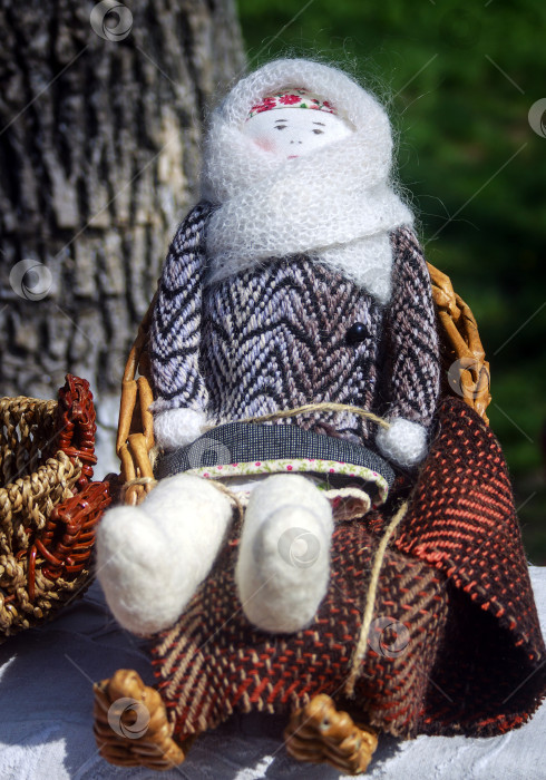 Скачать Национальная русская маленькая кукла ручной работы в зимней одежде сидит на плетеных санях фотосток Ozero