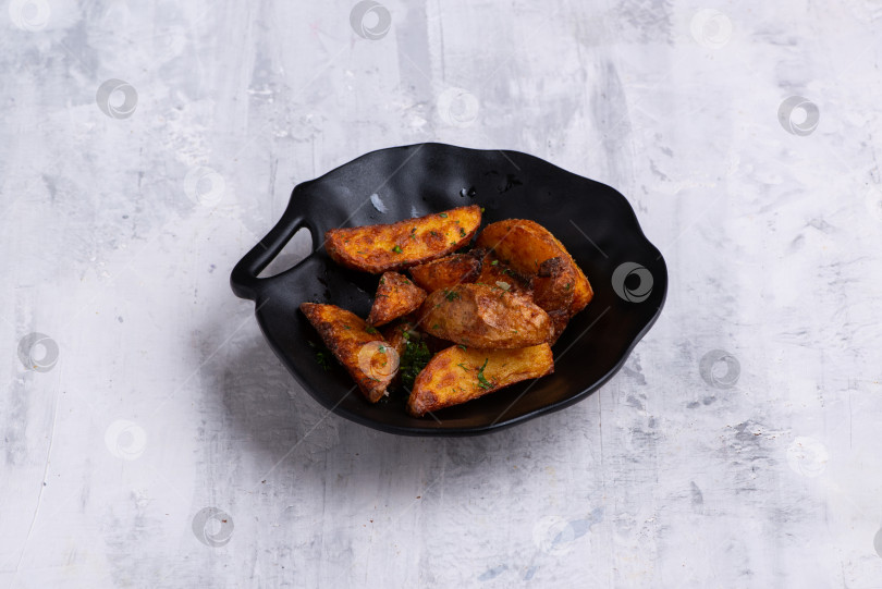 Скачать Снимок крупным планом вкусных картофельных дольок на черном блюде на белой мраморной поверхности фотосток Ozero