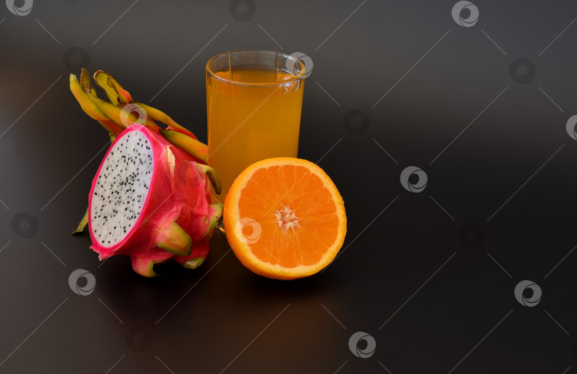 Скачать Высокий стакан с апельсиновым соком и питайей на черном фоне, рядом с половинками спелых фруктов. фотосток Ozero