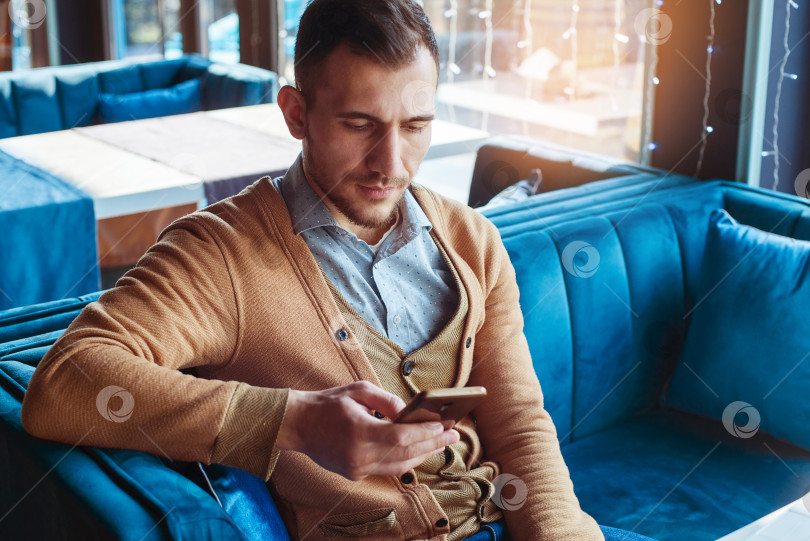Скачать Современный молодой человек сидит в кафе и держит в руках мобильный телефон. фотосток Ozero