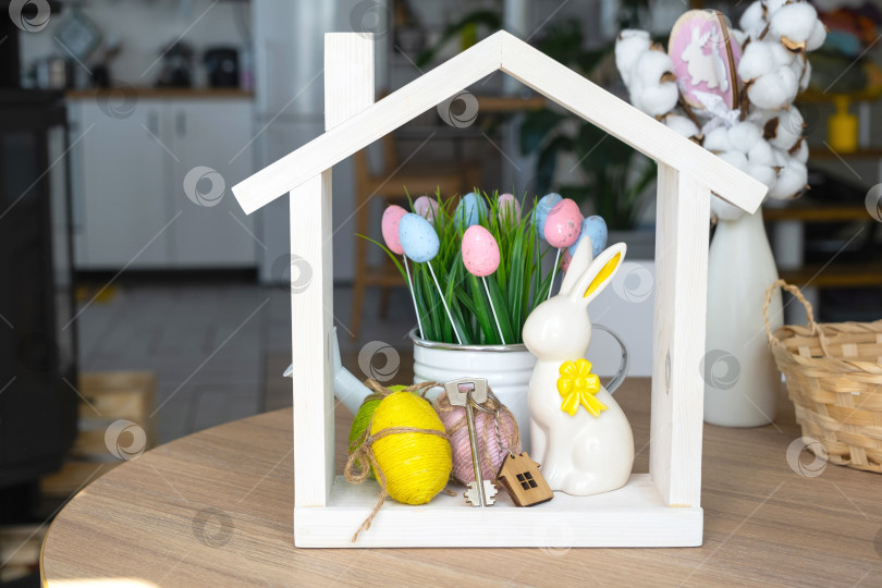 Скачать Ключ и крошечный домик уютного дома с пасхальным декором с кроликом и яйцами на кухонном столе. Строительство, дизайн, проект, переезд в новый дом, ипотека, страхование, аренда и покупка недвижимости фотосток Ozero