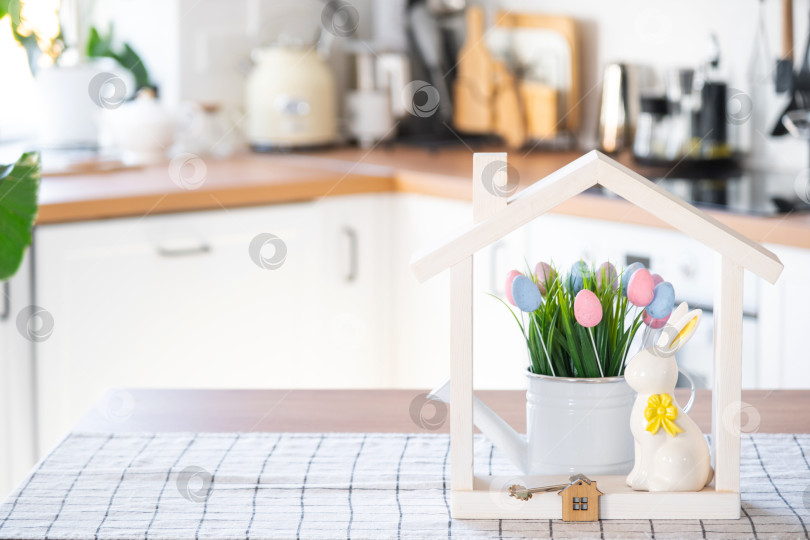 Скачать Ключ и крошечный домик уютного дома с пасхальным декором с кроликом и яйцами на кухонном столе. Строительство, дизайн, проект, переезд в новый дом, ипотека, страхование, аренда и покупка недвижимости фотосток Ozero