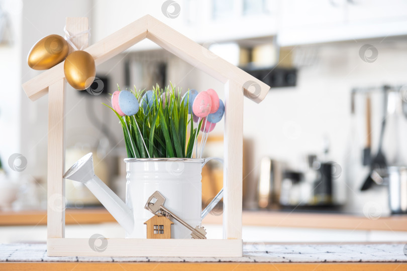 Скачать Ключ и крошечный домик уютного дома с пасхальным декором с цветными яйцами на кухонном столе. Строительство, дизайн, проект, переезд в новый дом, ипотека, страхование, аренда и покупка недвижимости фотосток Ozero