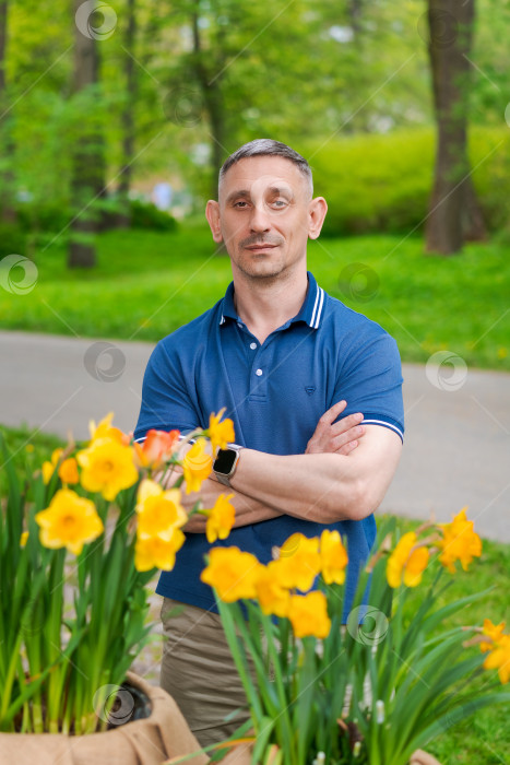 Скачать Мужчина в синей рубашке стоит перед клумбой с желтыми цветами фотосток Ozero