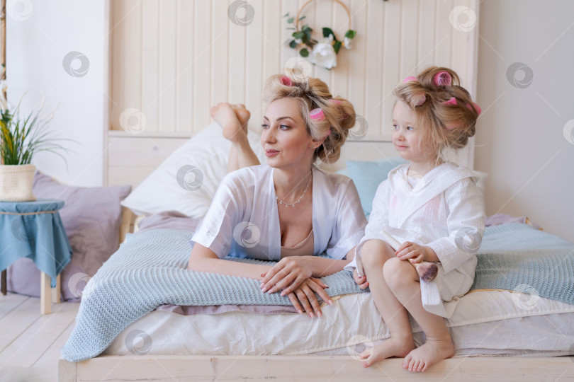 Скачать Мать и дочь лежат на кровати, волосы матери накручены на бигуди фотосток Ozero