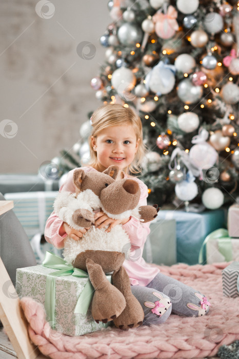 Скачать Девочка сидит возле рождественской елки и обнимает куклу-волка в шкуре медведя. фотосток Ozero
