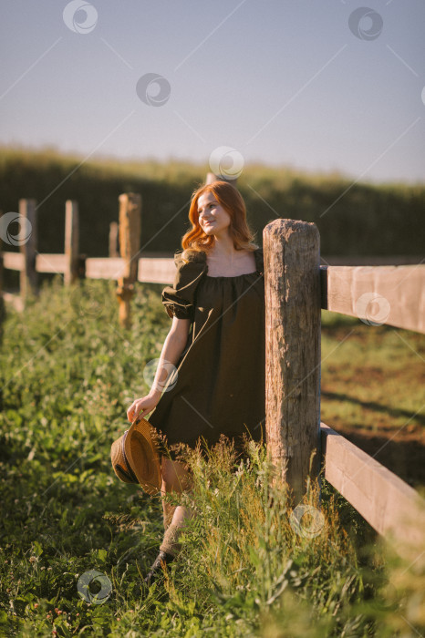 Скачать Красивая рыжеволосая девушка стоит возле массивного деревянного забора 3248. фотосток Ozero