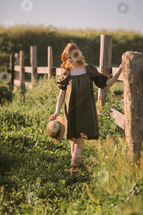 Скачать Красивая рыжеволосая девушка стоит возле массивного деревянного забора 3246. фотосток Ozero