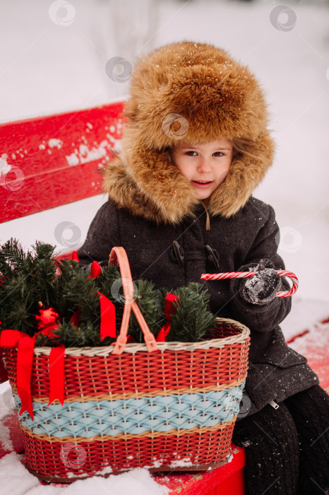 Скачать Ребенок с корзинкой сидит на красной скамейке зимой 3126 года. фотосток Ozero