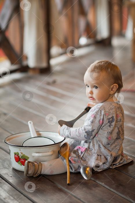 Скачать Годовалый ребенок играет на деревянном полу с кухонными принадлежностями 3450. фотосток Ozero