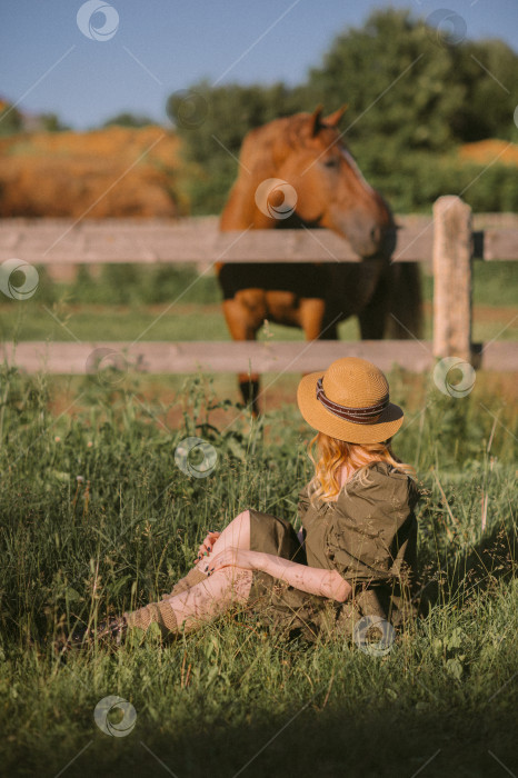 Скачать Рыжеволосая девушка сидит в траве рядом с пасущимися лошадьми 3240. фотосток Ozero